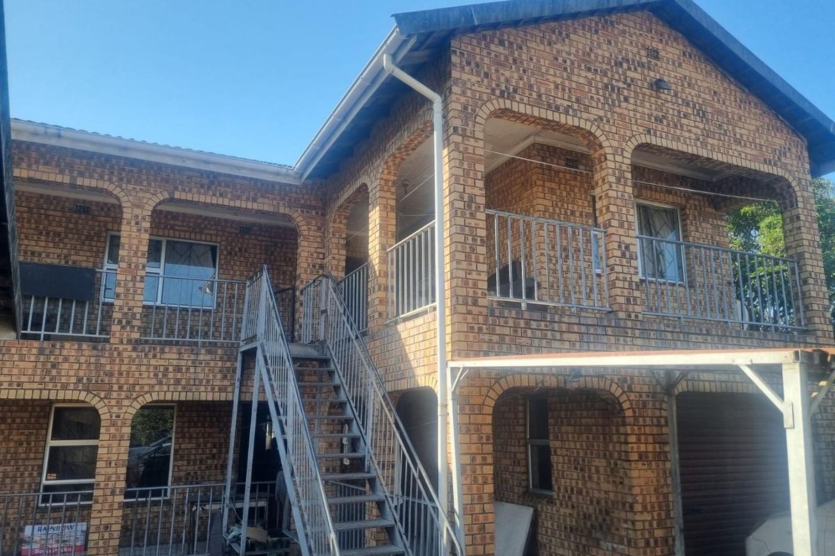 A two-story face brick retail or residential building featuring external metal staircases, covered balconies, and metal safety railings.