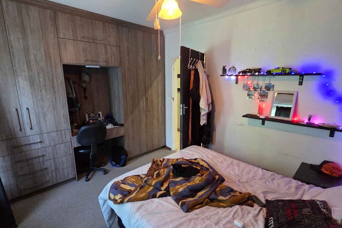 A bedroom featuring built-in wooden cabinetry with an integrated desk area, carpeted flooring, and a ceiling fan.