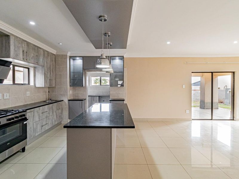 Modern open-plan kitchen featuring a central island, granite countertops, built-in gas hob, and sleek cabinetry, flowing seamlessly into the living area.