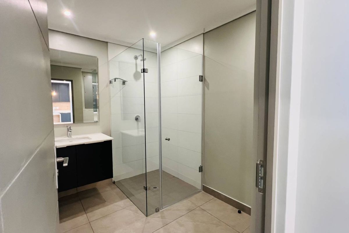 Modern bathroom featuring a glass-enclosed walk-in shower, wall-mounted vanity with basin, and neutral floor tiling.
