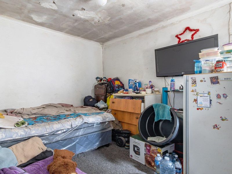 A bedroom space requiring significant maintenance, featuring visible ceiling damage and wall surface deterioration.