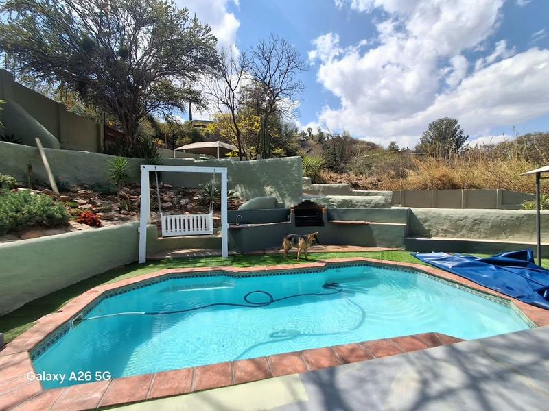 Outdoor pool area featuring a swimming pool, built-in braai, and tiered retaining walls with landscaped garden elements.