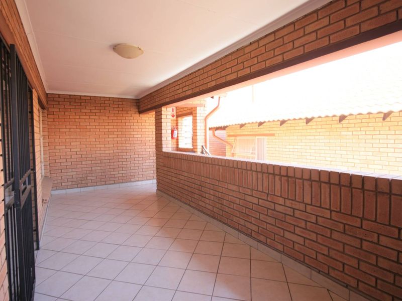 A spacious covered balcony featuring exposed brick walls and tiled flooring, providing a functional outdoor area.
