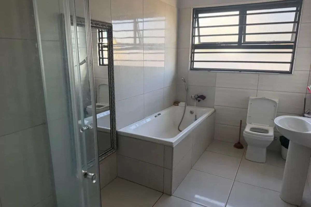 A clean, modern bathroom featuring a built-in bathtub, pedestal sink, toilet, and a separate glass-enclosed shower with neutral floor-to-ceiling tiling.
