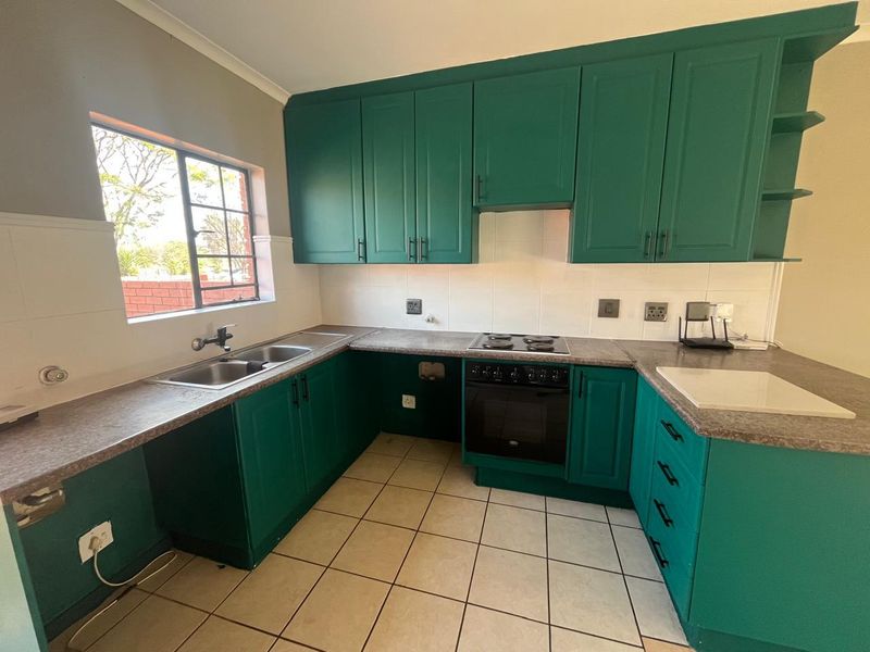 A functional kitchen featuring green cabinetry, laminate countertops, a built-in oven and hob, and tiled flooring with a window providing natural light.