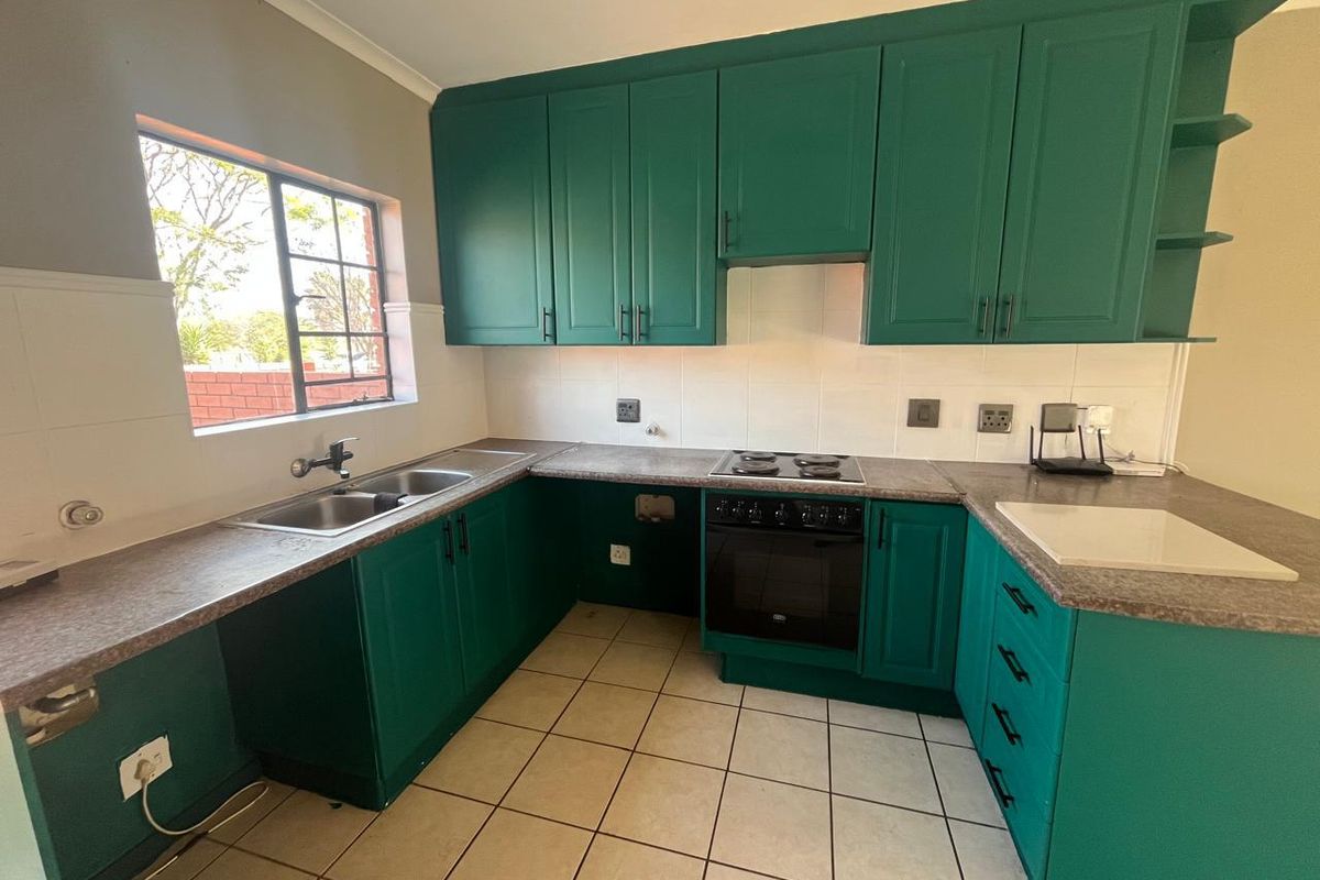 A functional kitchen featuring green cabinetry, laminate countertops, a built-in oven and hob, and tiled flooring with a window providing natural light.