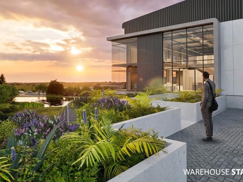 Architectural rendering of a modern industrial warehouse facility featuring glass facade, concrete planters, and paved exterior area at sunset.