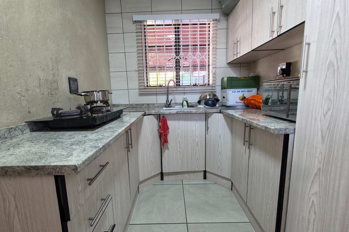 Compact kitchen featuring laminate cabinetry, stone-look countertops, tiled backsplash, and a stainless steel sink with a window overlooking the exterior.