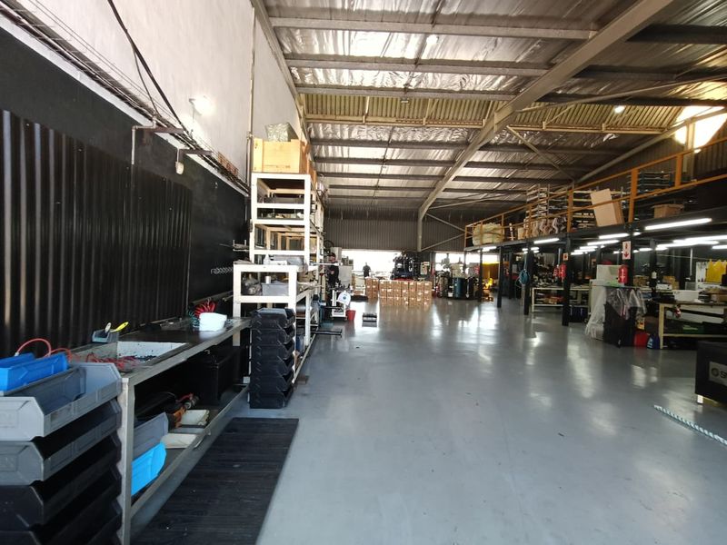 Spacious industrial warehouse featuring high ceilings with exposed steel trusses, a mezzanine level, and durable epoxy-coated concrete flooring suitable for various commercial operations.