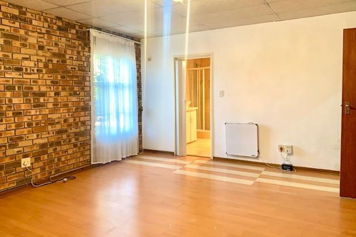 Spacious bedroom featuring an exposed brick accent wall, laminate flooring, and an en-suite bathroom access.
