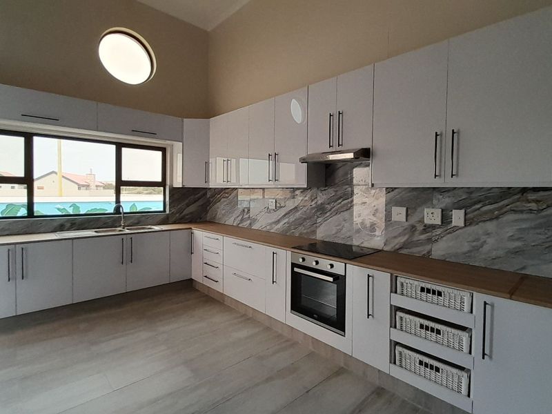 Modern kitchen featuring white cabinetry, marble-look splashbacks, wooden countertops, built-in oven, electric hob, and stainless steel sink with ample natural light.