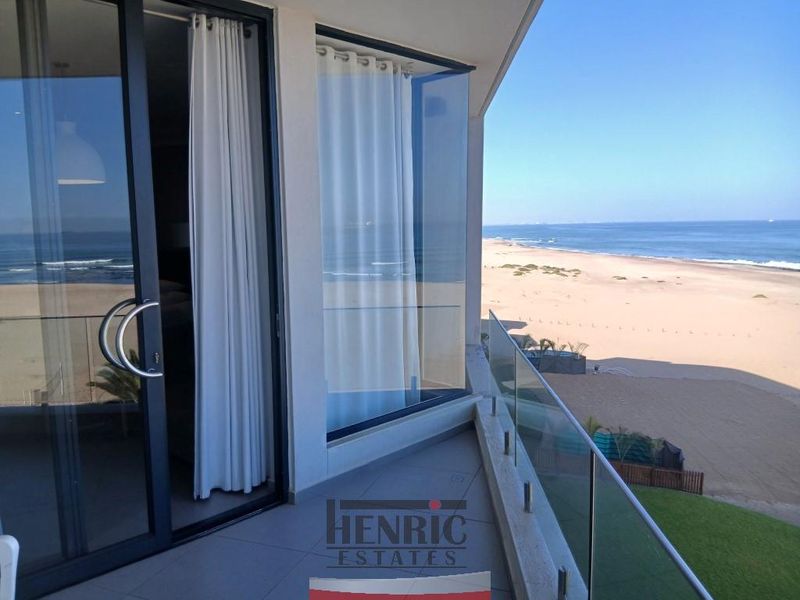 A modern balcony featuring a glass balustrade and sliding door access, offering expansive, unobstructed views of the beach and ocean.