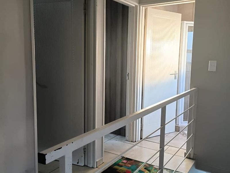 A functional upper-level hallway featuring tiled flooring and a white metal balustrade, providing access to multiple rooms.