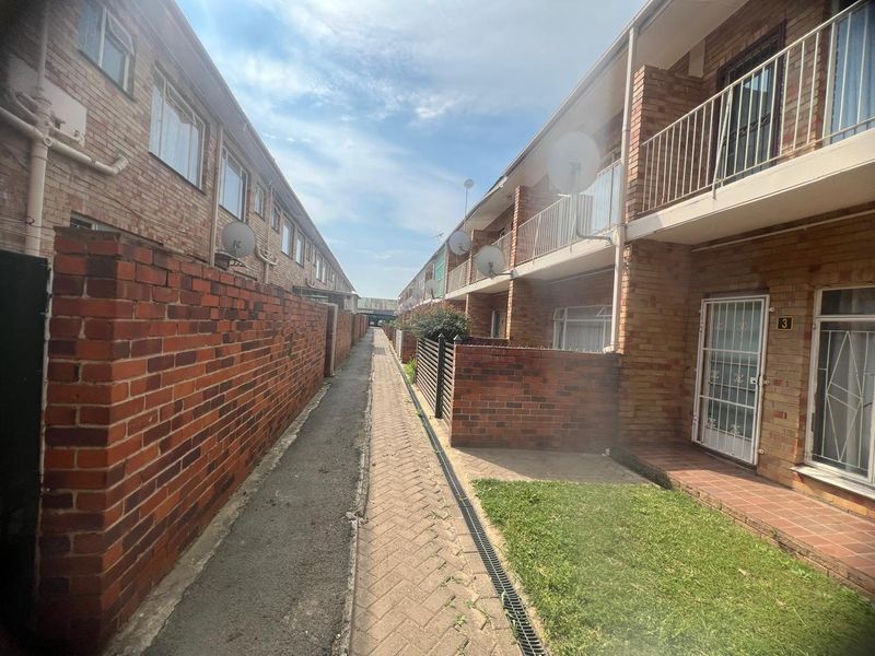 Exterior view of an apartment complex showing a paved walkway between brick buildings with ground floor entrances and upper-level balconies.
