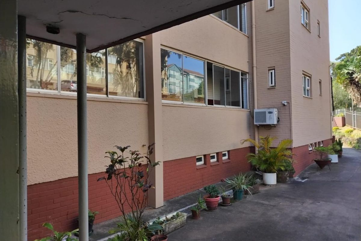 Rear exterior view of the apartment building featuring brick and plaster facade, sliding windows, and a covered walkway area.