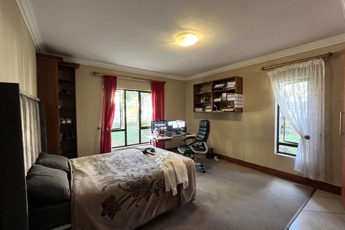 Spacious bedroom featuring built-in shelving, large windows with garden views, and neutral wall finishes.