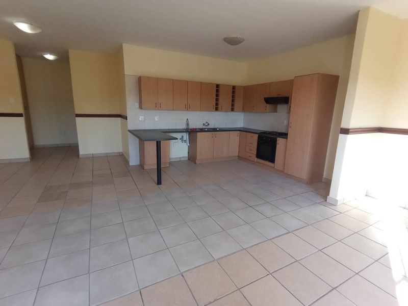 An open-plan kitchen area featuring light wood cabinetry, a breakfast bar, and tiled flooring, presenting a functional space ready for modern updates.