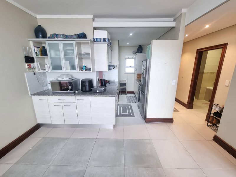 A functional kitchen featuring built-in cabinetry, granite countertops, and tiled flooring, with an adjacent hallway leading to a bathroom.