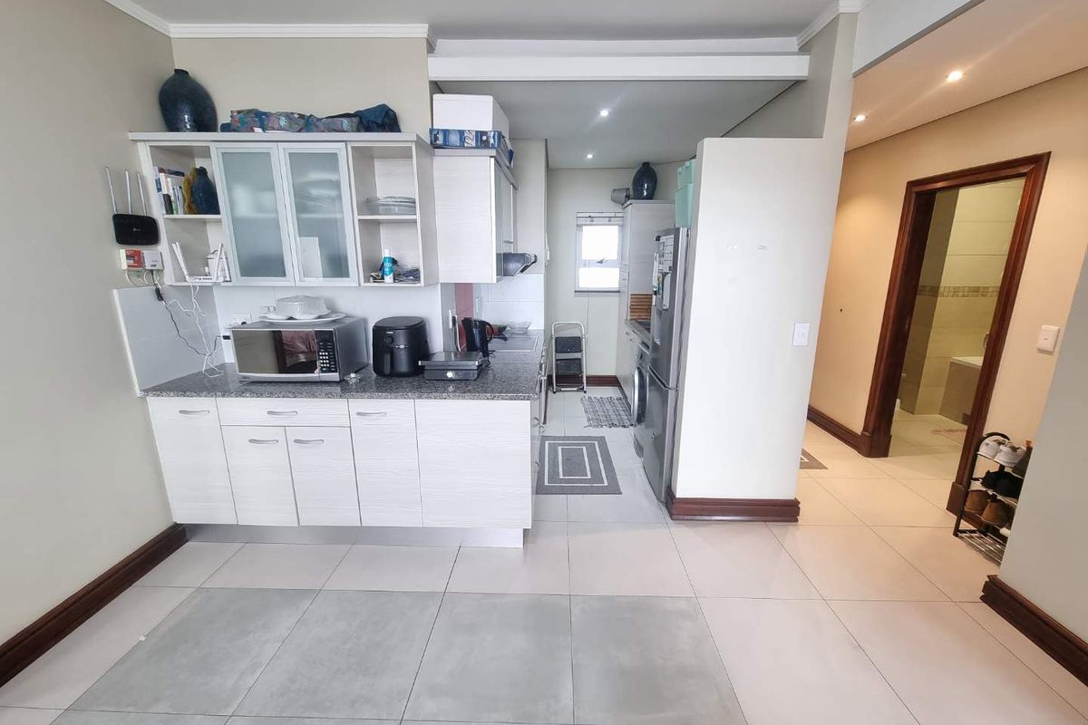 A functional kitchen featuring built-in cabinetry, granite countertops, and tiled flooring, with an adjacent hallway leading to a bathroom.