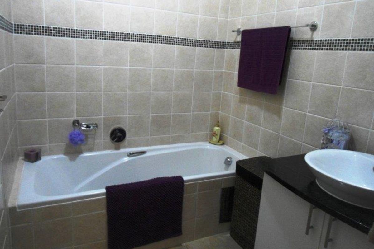 A functional bathroom featuring a built-in bathtub with wall-mounted mixer, tiled walls with decorative border, and a vanity cabinet with a vessel sink.