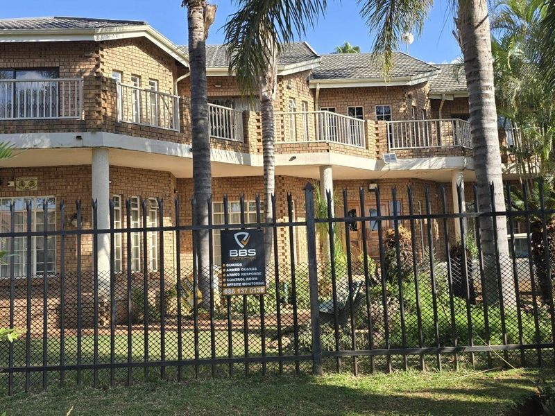 Front view of a double-story face brick residential building featuring upper-level balconies with metal railings and secure perimeter fencing.
