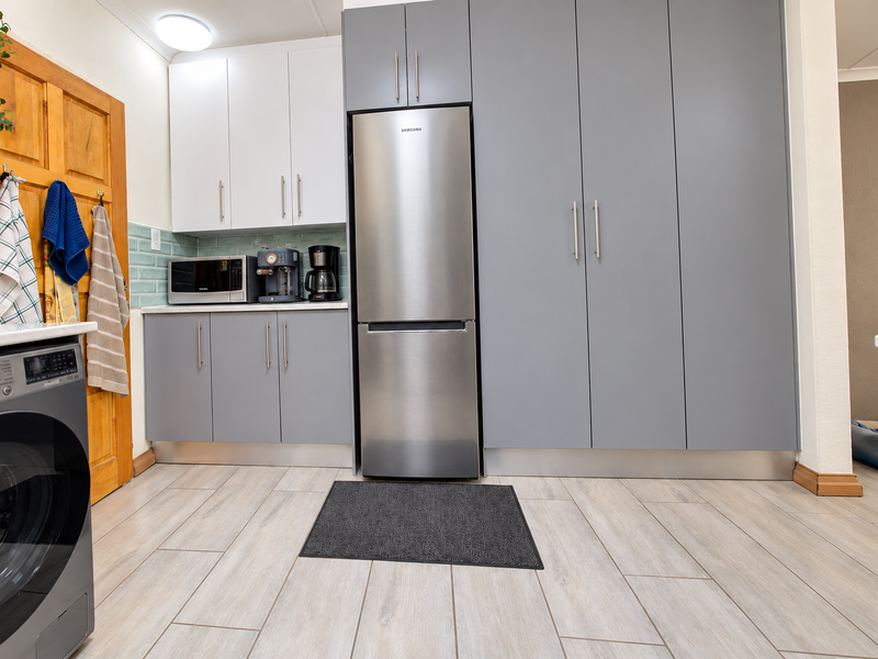 Modern kitchen area featuring sleek grey and white cabinetry, tiled backsplash, and integrated laundry facilities with light wood-look tiled flooring.