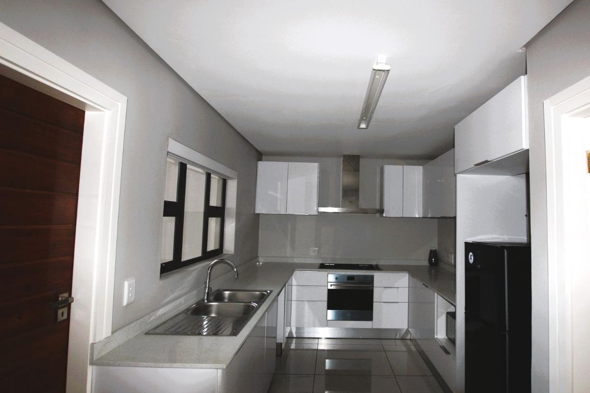 Modern kitchen featuring white high-gloss cabinetry, stone countertops, stainless steel double sink, built-in oven, hob, and extractor fan with tiled flooring.
