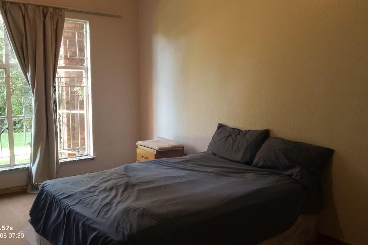 A bedroom featuring a large window with security bars, neutral wall finishes, and carpeted flooring.