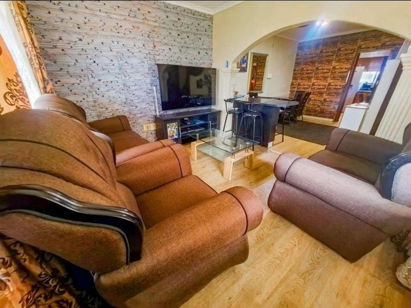 A living room featuring a stone-cladding accent wall, laminate flooring, and an open-plan layout connecting to a breakfast bar area.