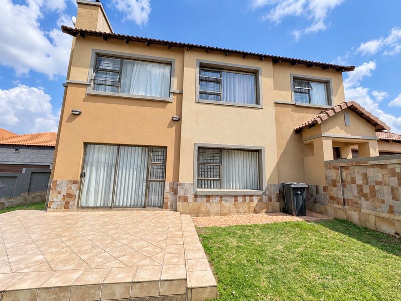 Rear view of a two-story house featuring a tiled patio, stone-clad base, and aluminium-framed windows with a small private garden area.
