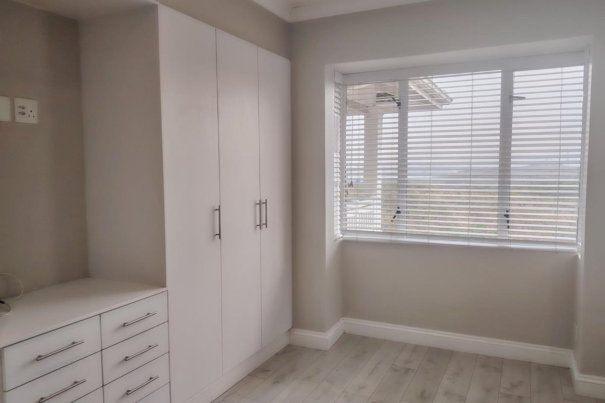 A bright, modern bedroom featuring extensive built-in cabinetry with integrated drawers, light-toned laminate flooring, and venetian blinds.