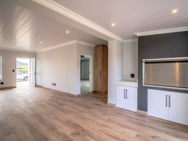 Spacious living area featuring modern laminate flooring, recessed lighting, a built-in braai, and custom cabinetry, offering a clean and versatile open-plan space.