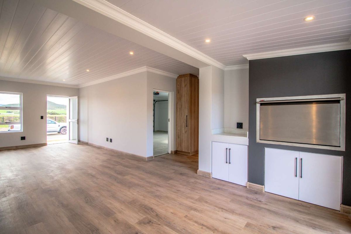 Spacious living area featuring modern laminate flooring, recessed lighting, a built-in braai, and custom cabinetry, offering a clean and versatile open-plan space.