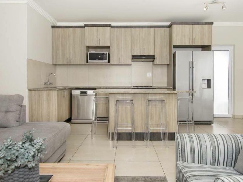 Modern open-plan kitchen featuring light wood cabinetry, stone countertops, integrated appliances, and a breakfast bar, seamlessly flowing into the living area.