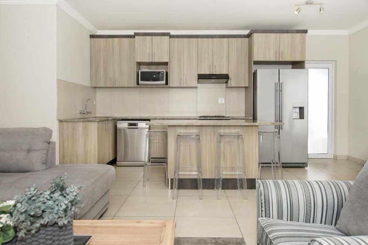 Modern open-plan kitchen featuring light wood cabinetry, stone countertops, integrated appliances, and a breakfast bar, seamlessly flowing into the living area.