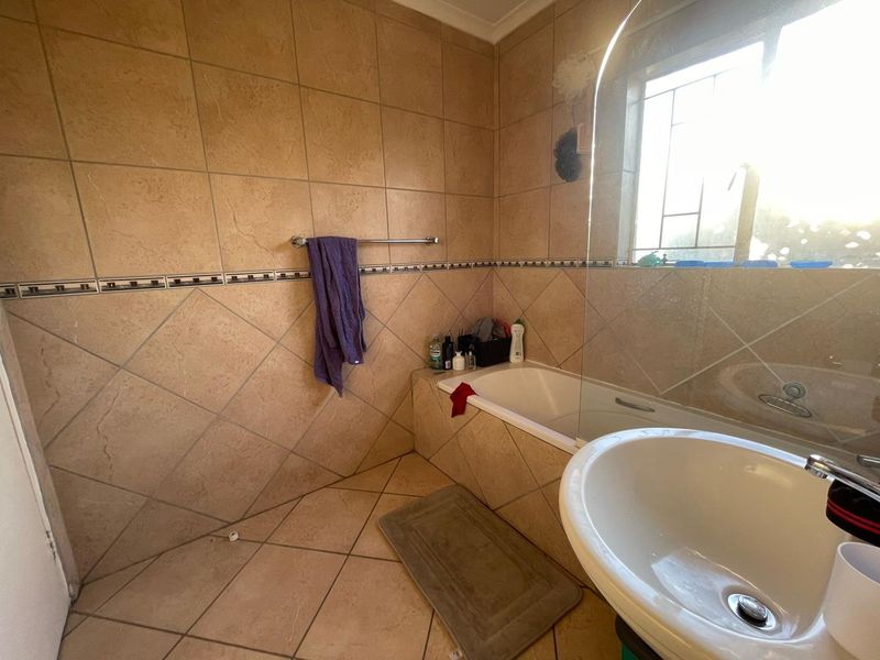 A functional bathroom featuring a built-in bathtub with a glass shower screen, pedestal washbasin, and neutral ceramic wall and floor tiling.