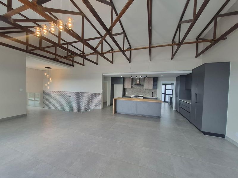 Spacious open-plan living area featuring high exposed timber trusses, a modern kitchen with island, and contemporary finishes throughout.