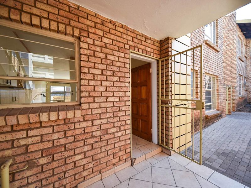 Entrance area featuring exposed brickwork, a security gate, and tiled flooring leading to a timber front door.