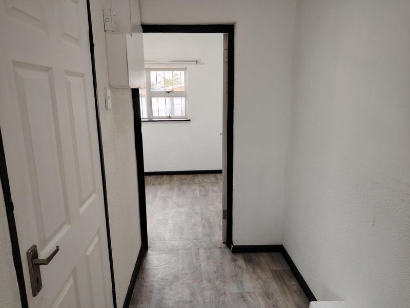 A simple hallway connecting to an adjacent room, featuring neutral laminate flooring and white walls with dark trim accents.