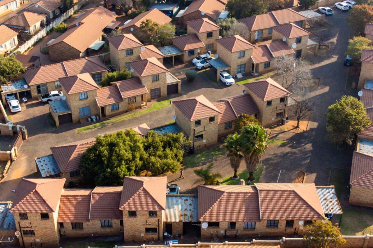 Aerial view of a residential apartment complex featuring multiple brick units with tiled roofs, paved driveways, and established communal landscaping.