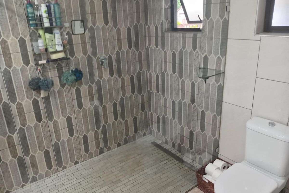 A modern bathroom featuring a walk-in shower with decorative geometric wall tiles, a glass shelf, and a white toilet.