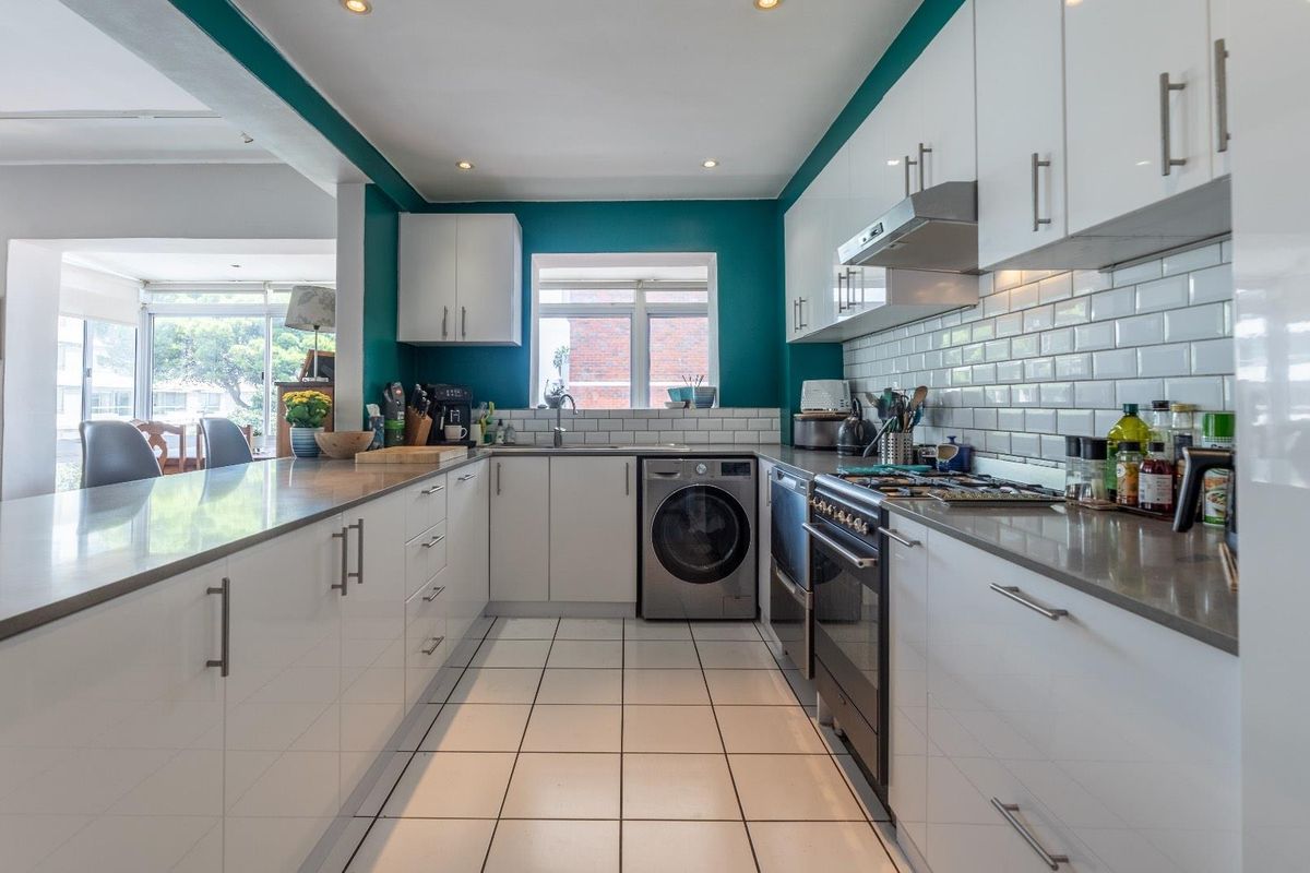 Modern galley-style kitchen featuring white cabinetry, stone countertops, subway tile backsplash, integrated oven, and a built-in washing machine.