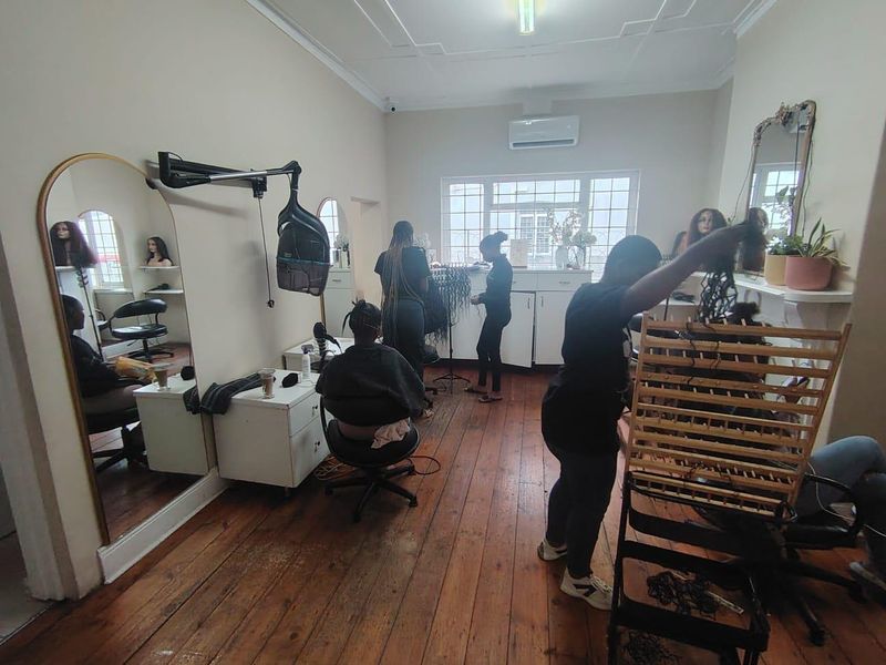 A functional office space featuring hardwood flooring, built-in cabinetry, and a wall-mounted air conditioning unit, currently utilized as a salon.