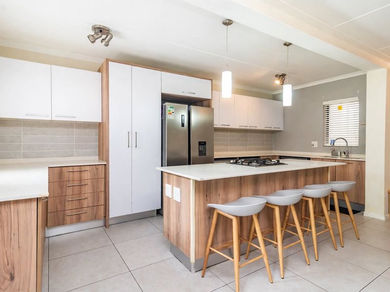 Modern kitchen featuring a central island with a gas hob, ample built-in cabinetry, tiled flooring, and a sleek tiled backsplash.