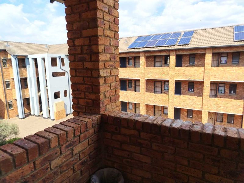 A view from a brick-walled balcony overlooking the apartment complex courtyard, featuring solar panels installed on the roof.