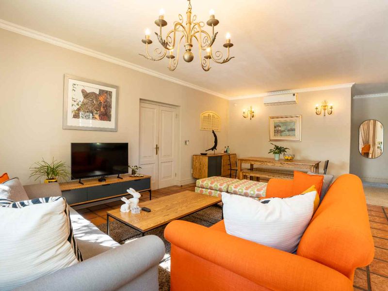 Spacious living room featuring terracotta floor tiles, coved cornicing, a decorative chandelier, wall sconces, and a wall-mounted split-system air conditioner.