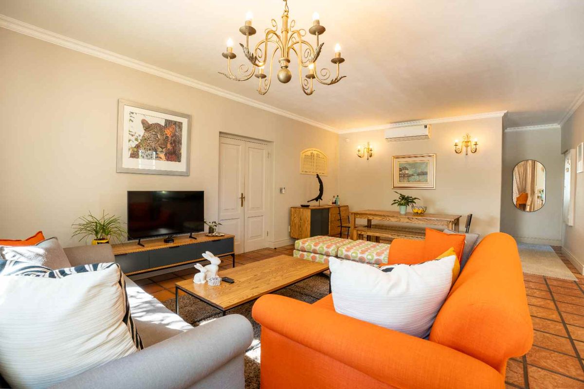 Spacious living room featuring terracotta floor tiles, coved cornicing, a decorative chandelier, wall sconces, and a wall-mounted split-system air conditioner.