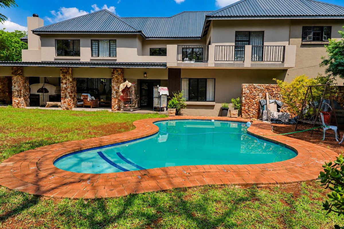 Rear view of a two-story house featuring a swimming pool with brick coping, a covered patio area, and an upper-level balcony.