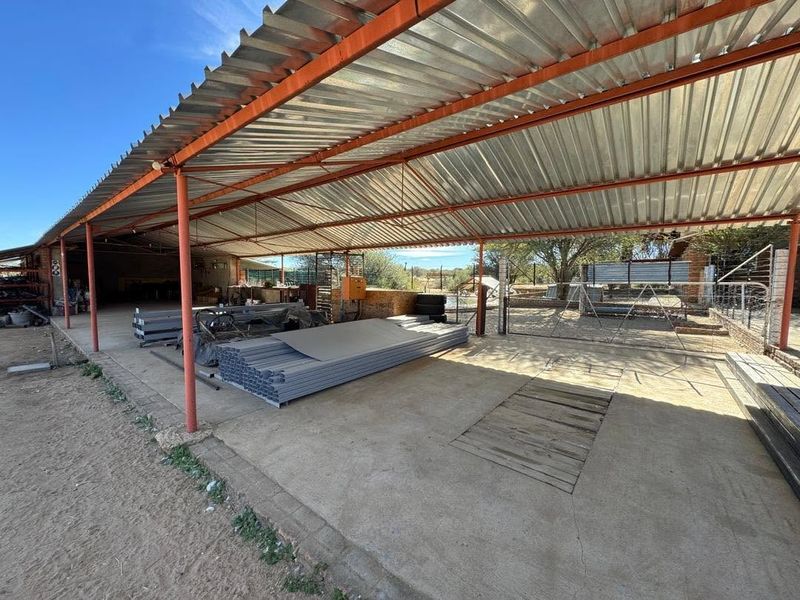 A large, open-sided utility shed or workshop area featuring a corrugated metal roof, steel support structure, and concrete flooring, suitable for storage or farm operations.