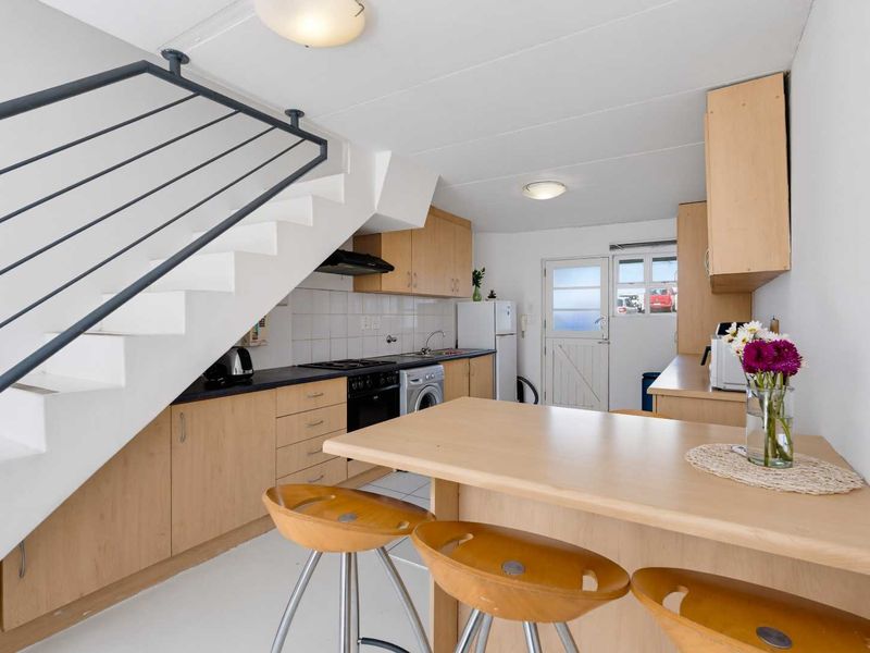 Compact kitchen featuring light wood cabinetry, built-in oven, gas hob, and a breakfast bar, situated beneath an open staircase.
